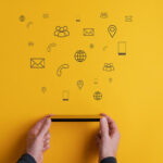 Hands holding a smartphone with digital communication icons floating above on a yellow background, representing marketing and connectivity.