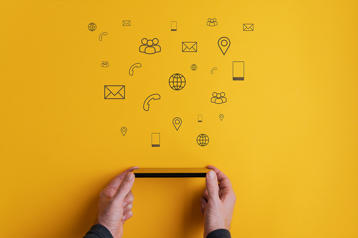 Hands holding a smartphone with digital communication icons floating above on a yellow background, representing marketing and connectivity.