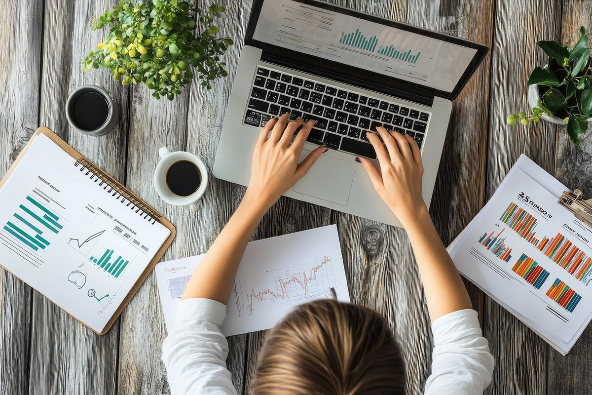 Top-down view of a person analyzing digital marketing data on a laptop, surrounded by printed charts and graphs, symbolizing AI-driven orthopedic marketing trends.